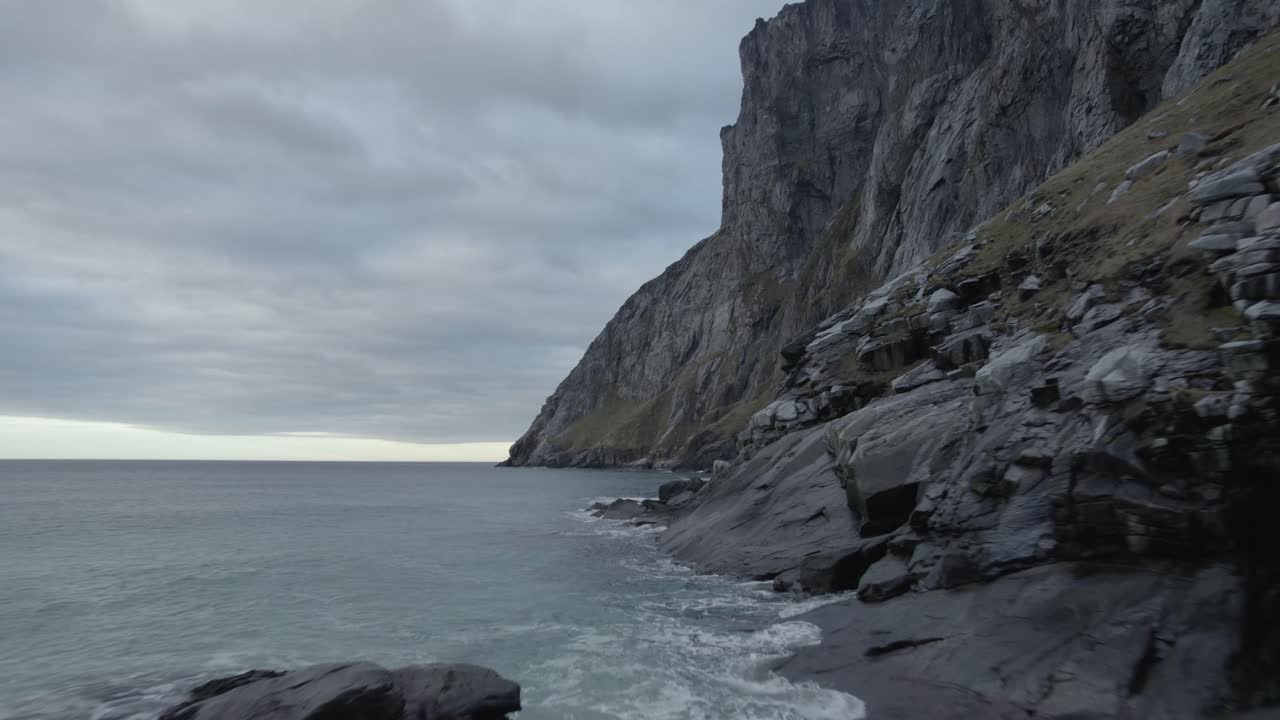 vista aérea de drones a baja altura sobre la costa rocosa, bajo montañas empinadas, tarde sombría, en lofoten, noruega