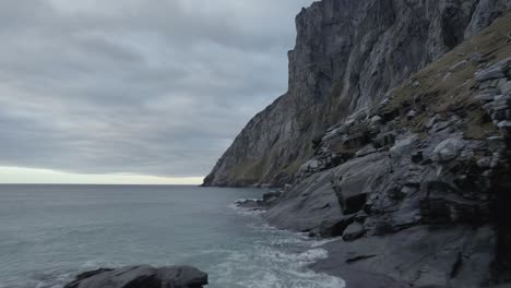 Vista-Aérea-De-Drones-A-Baja-Altura-Sobre-La-Costa-Rocosa,-Bajo-Montañas-Empinadas,-Tarde-Sombría,-En-Lofoten,-Noruega