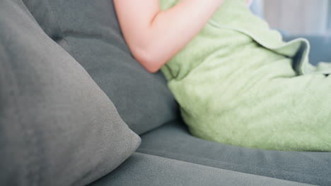 close up view of woman wrapped in green towel seated on soft gray couch, highlighting fabric texture and casual post-bath relaxation moment in bright cozy indoor environment with minimal background