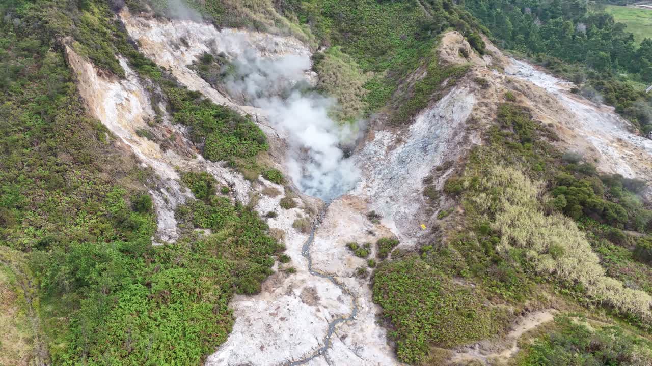 Scenic drone video capturing volcanic sulfur emissions and fumaroles in a geothermal crater, surrounded by lush vegetation and rugged terrain. Sikidang Crater, Dieng, Indonesia