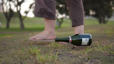 dramatic slow motion shot of a socially irresponsible person tossing an empty wine bottle on the ground whilst walking in a public park