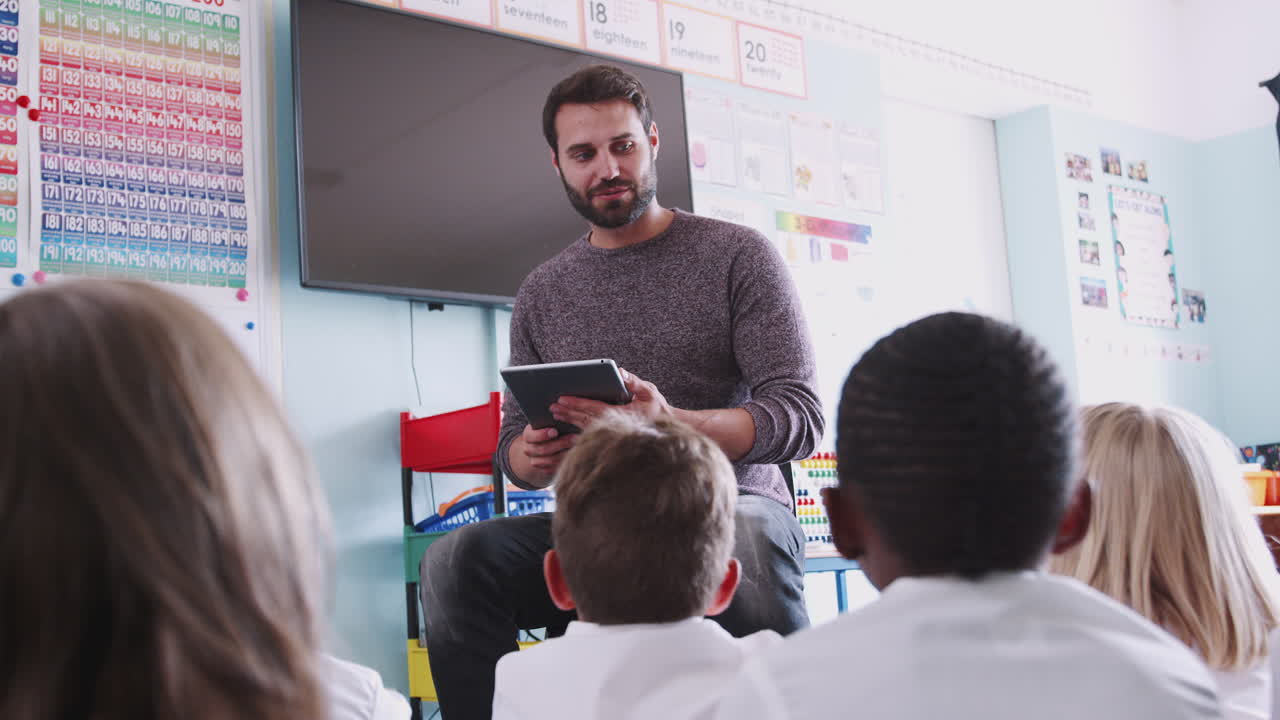 maestro de sexo masculino leyendo una historia a un grupo de alumnos de primaria vestidos con uniforme en el aula de la escuela