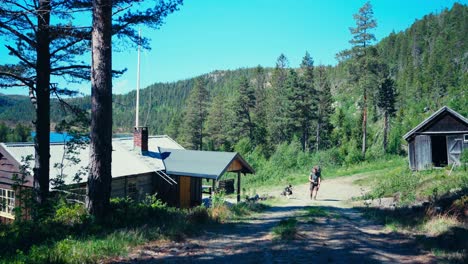 Portrait-Of-Backpacker-With-His-Dog-Near-Mountain-Cabin-During-Summer