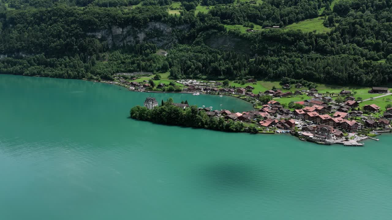 Aerial of the beutiful small village of Iseltwald at the turquoise lake Brienzersee surrounded by the alp mountainens showing Castle seeburg and revealing da distant view near Interlaken Switzerland