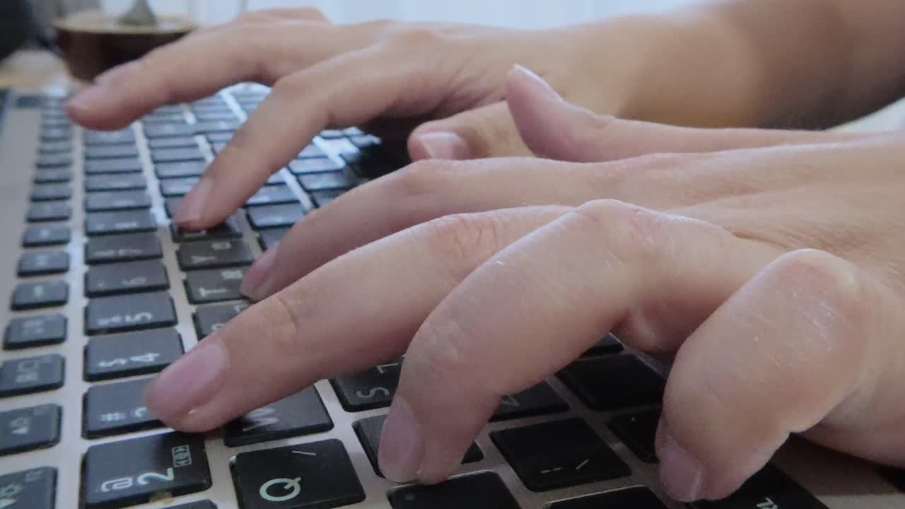 Detailed side view close-up of female hands interacting with a laptop keyboard, fingers pressing keys