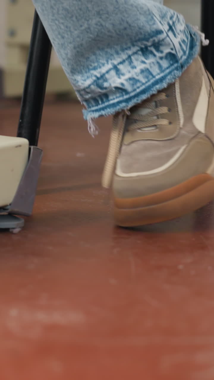 zapatilla con dobladillo de denim deshilachado sobre el suelo, primer plano del interior de un estudio tranquilo de la suela y los cordones de una zapatilla beige, estudiante relajado dando golpecitos con el pie bajo la silla, tonos cálidos y suelo pintado texturizado, natural