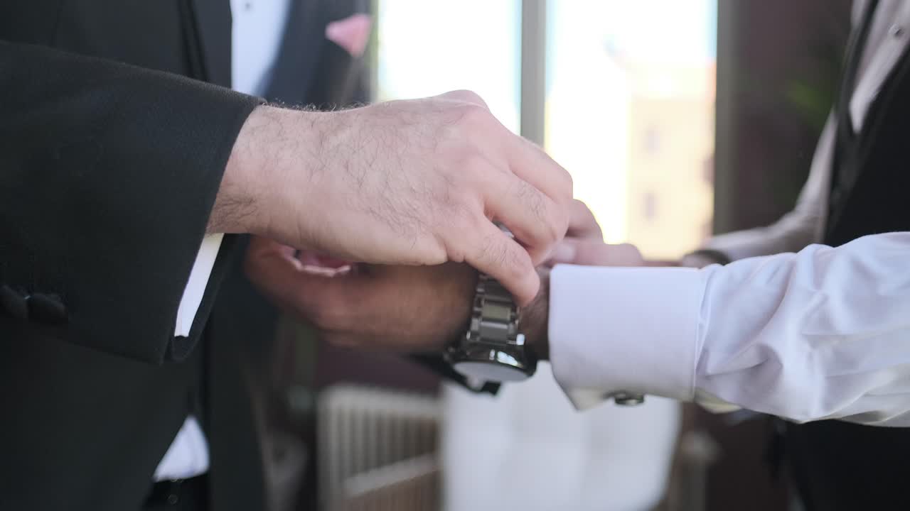A groom dresses and someone adjusts his watch, preparing for a wedding-1