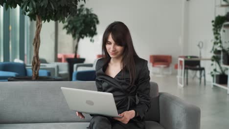 young,-beautiful-woman-in-a-suit-gestures-goodbye,-greets,-and-gives-a-high-five-while-speaking-on-a-video-call-through-a-laptop