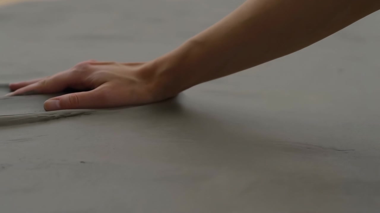 Mano de una persona moviéndose sobre una superficie de material plano texturizado, desde una perspectiva de arriba hacia abajo, con detalles en gris y tono de piel.