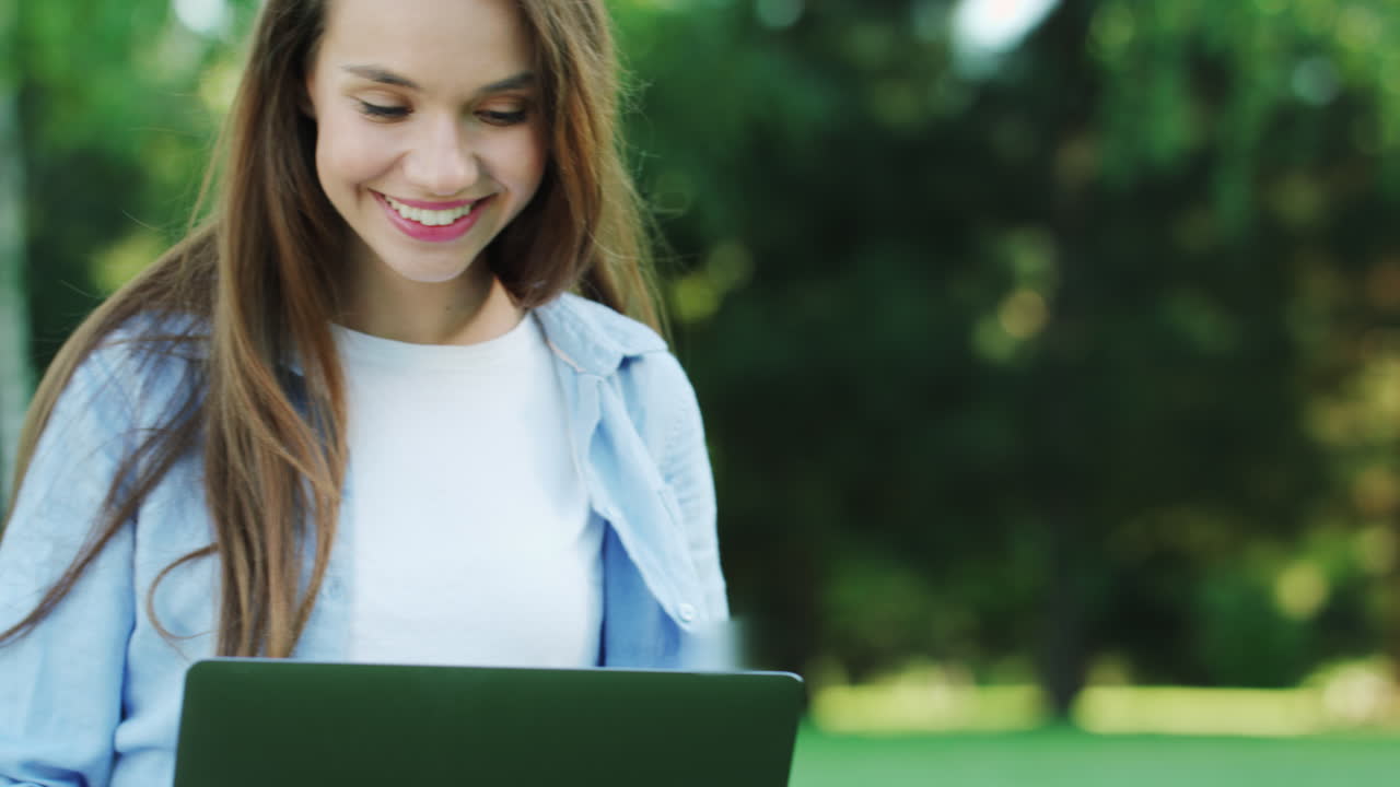 mujer sonriente trabajando en una computadora portátil en el parque de la ciudad en un día de verano