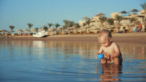 Bebé-Gordito-Jugando-Con-Juguete-En-Agua-De-Mar.-Niño-Salpicando-Agua-En-La-Playa