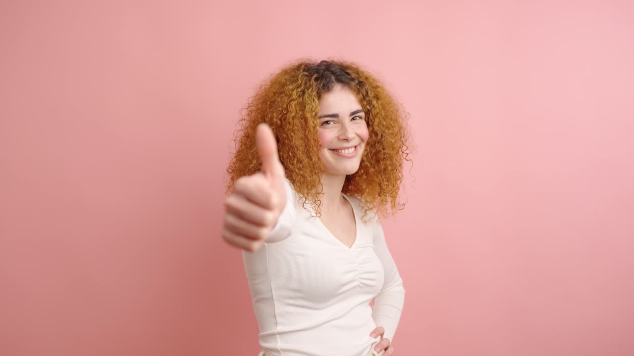 Enthusiastic young woman showing thumbs up on pink background