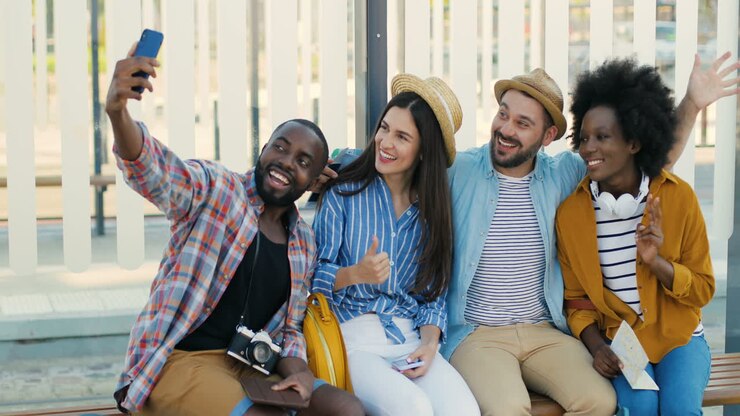 Multiethnic group of travellers sitting at bus sto, smiling and making a selfie