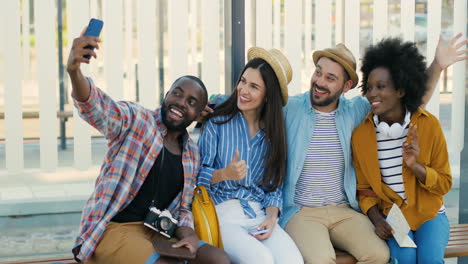 multiethnic group of travellers sitting at bus sto, smiling and making a selfie