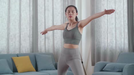 joven atleta asiática haciendo ejercicio, estirándose y practicando yoga en la postura del guerrero ii en casa. estilo de vida saludable, fitness, bienestar y concepto de atención plena