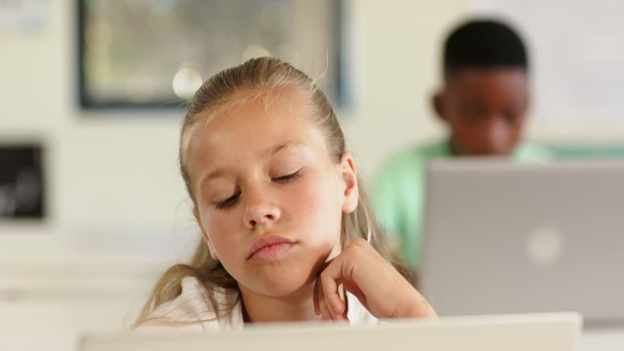 Alunni diversi con un bambino annoiato che riposa, guarda l'ora e picchietta il banco a scuola vicino a un laptop.