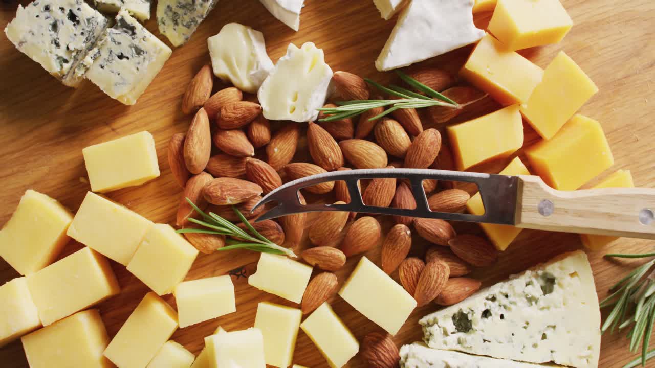 Video of assorted hard and soft cheeses, nuts and rosemary with knife on wooden board