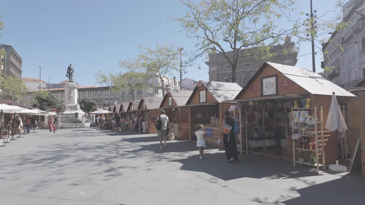 Outdoor market stalls in Porto’s Praça da Batalha with a statue and city buildings on a sunny day