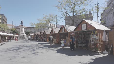 outdoor market stalls in porto’s praça da batalha with a statue and city buildings on a sunny day
