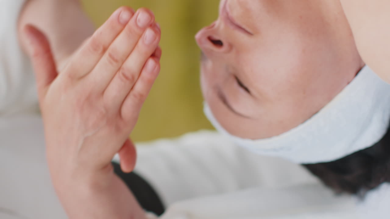 테라피스트 여성 의사는 여성이 휴식을 취하는 스파 얼굴 마사지를 산의 야외에서 손으로 만니다.