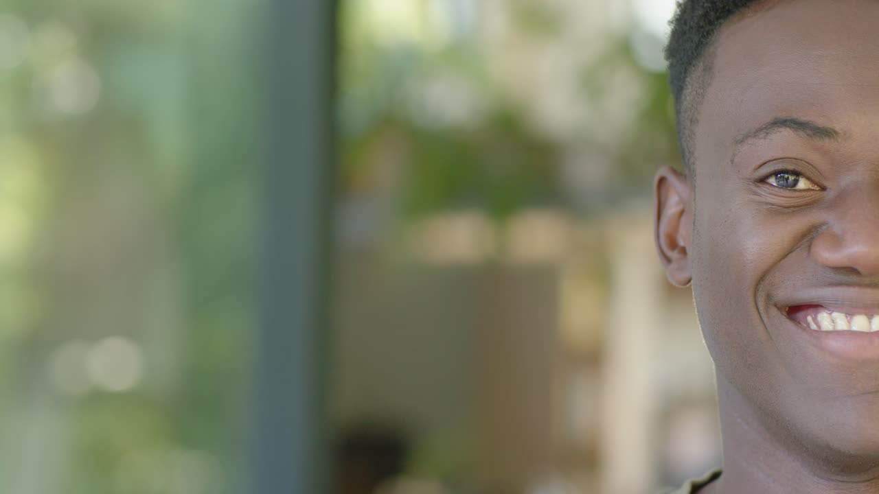 Man holding camera gaze, shifting neutral to broad smile by window wearing olive green top