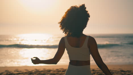 mulher praticando pilates com as mãos trancadas na praia ao nascer do sol em close-up orientado verticalmente