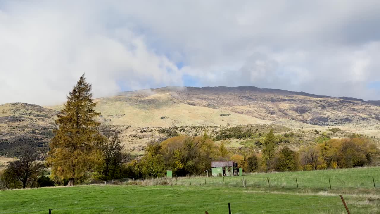 A serene drive through Wanaka, showcasing lush greenery, autumn foliage, and distant hills under a partly cloudy sky
