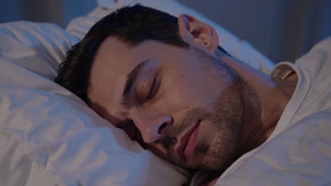 A serene video scene of a man sleeping peacefully under white sheets, captured from a close-up angle