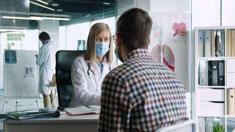 nahaufnahme einer ärztin mit medizinischer maske, die am schreibtisch sitzt und mit jungen patienten spricht, während sie eine behandlung verschreibt