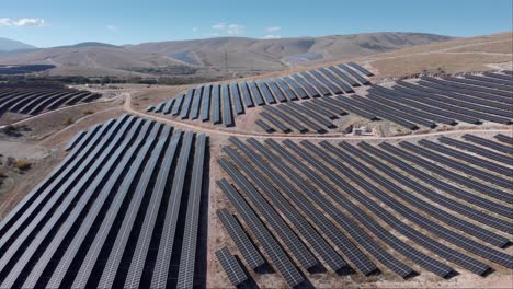 Drohne-über-Photovoltaik-Solarpark-Reihenpaneele-Ländliche-Hügel-Blauer-Himmel-Sonnig