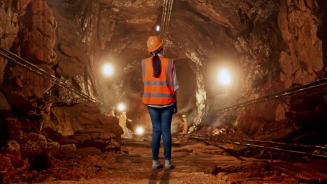 full body back view of asian female engineer with safety helmet talking on smartphone in underground mine tunnel