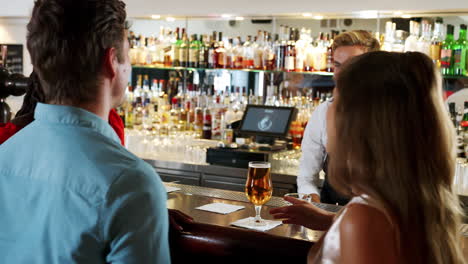 barman serving group of young friends meeting for drinks in cocktail bar