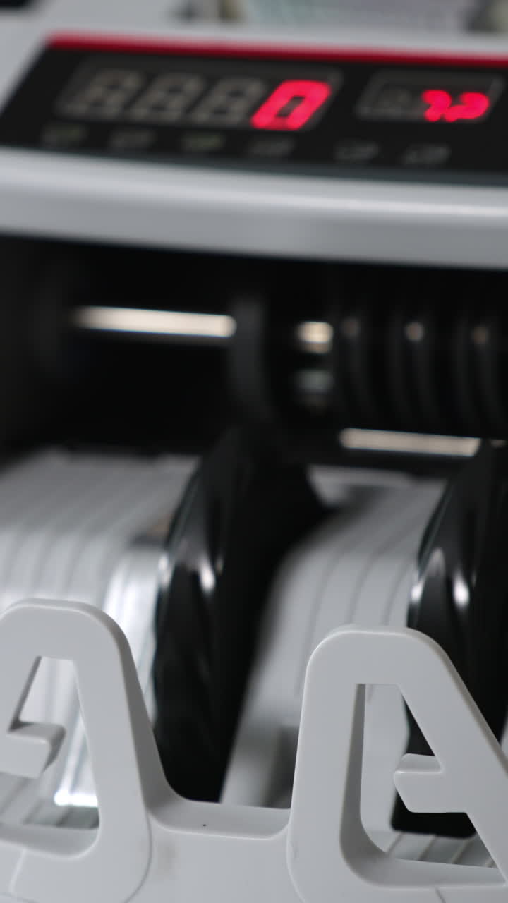 Cash counting machine switched on and the rollers begin to rotate. A wad of hundred dollar notes are placed into machine to be counted. Close up. Vertical video