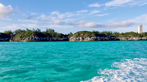 sailing with a boat in the turquoise ocean water near the rocky shore of blue lagoon island, bahamas