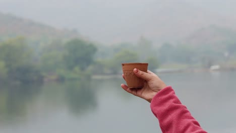 girl enjoying hot tea served in traditional pottery clay cup with blurred mountain lake landscape