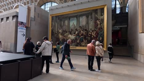 personas observando una gran pintura en el museo de parís