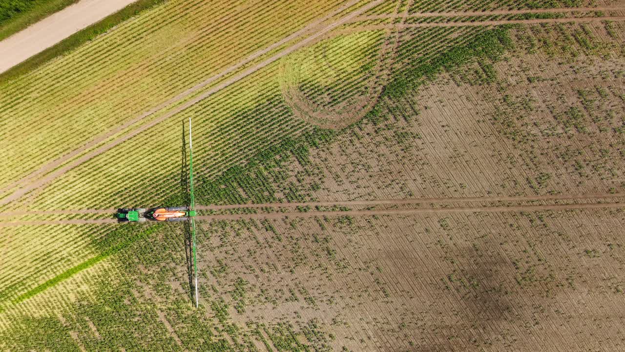 Dry brown farmland with visible tractor tire lines and spray trails in sunny summer weather
