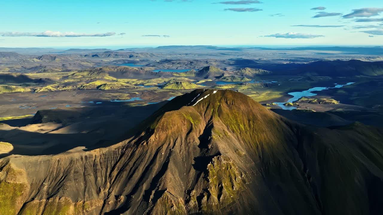 Epic aerial flight over Iceland’s towering volcanic peak, revealing vast sweeping plains, glowing crater slopes and distant shimmering lakes beneath powerful northern light
