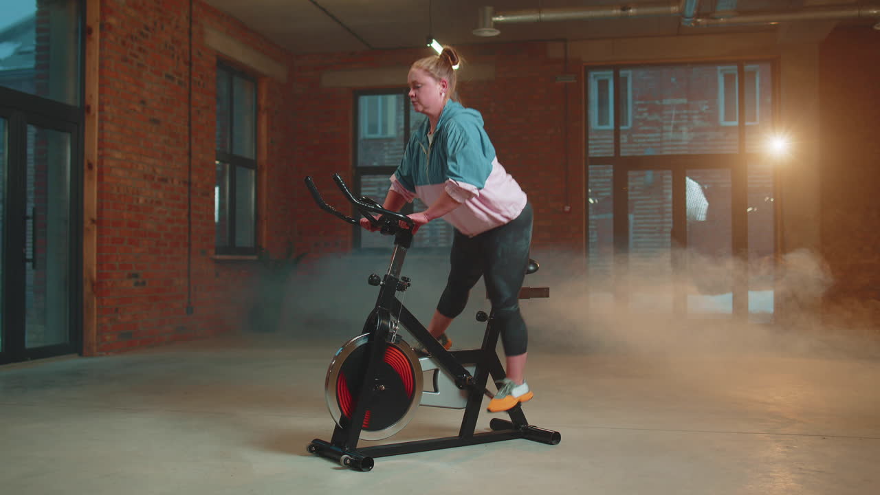 mujer atlética montando una bicicleta estacionaria de giro rutina de entrenamiento en el gimnasio de bruma, pérdida de peso en el interior