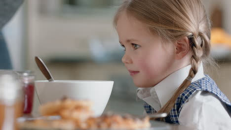 beautiful little girl eating breakfast in kitchen with father pouring milk into cereal bowl enjoying caring for daughter at home