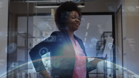 female professional standing in office holding laptop, displaying holographic finance data charts