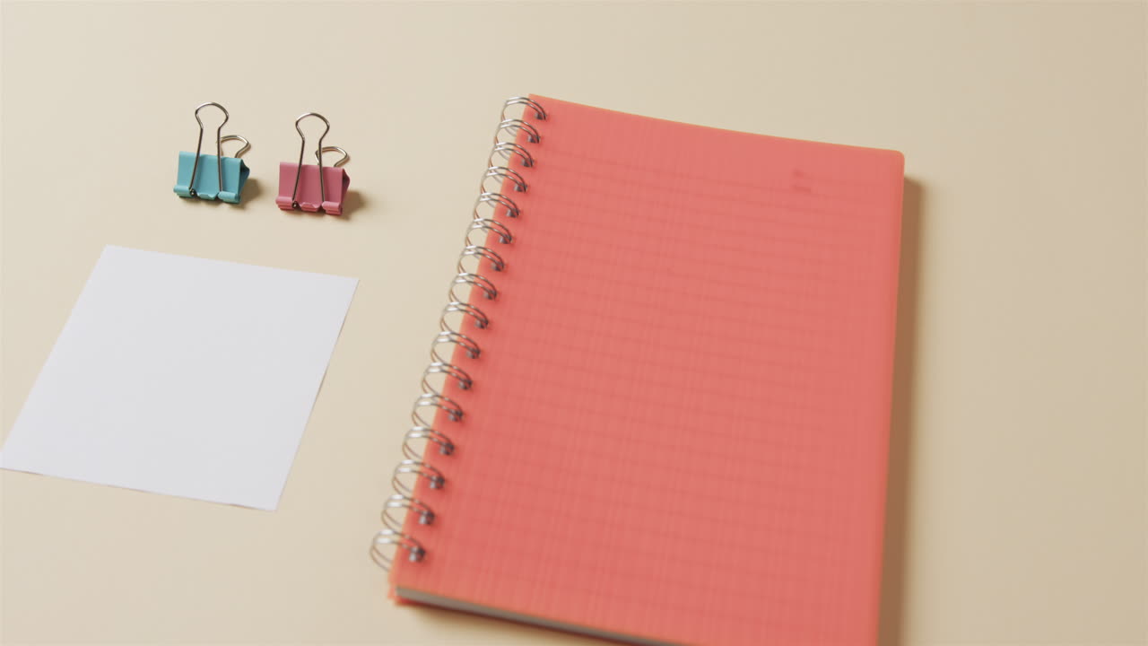 Close up of red notebook and school stationery arranged on beige background, in slow motion
