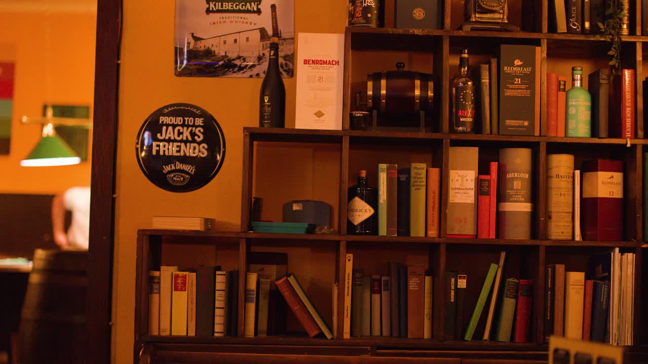 Inquadratura statica di un'accogliente libreria di un bar, bottiglie di whisky, libri, illuminazione calda, atmosfera da pub vintage