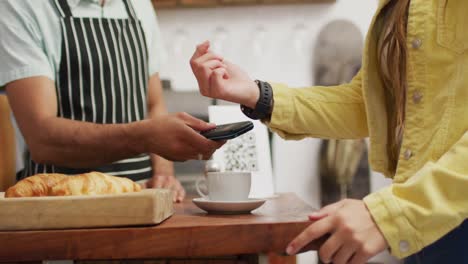 Vídeo-De-La-Sección-Media-De-Un-Vendedor-Masculino-Diverso-En-Una-Cafetería-Y-Un-Cliente-Pagando-Con-Un-Reloj-Inteligente