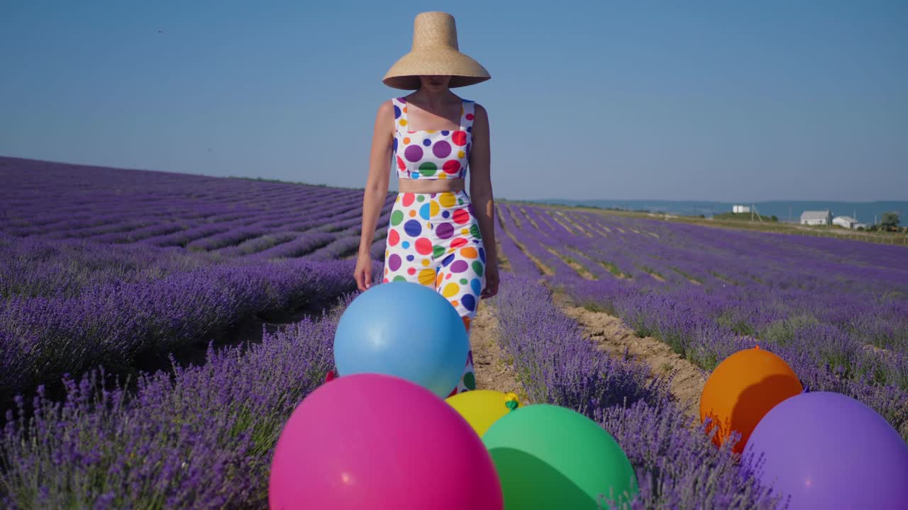 원과 모자를 가진 다채로운 의상을 입은 여자가 큰 부풀이 모자를 들고 있습니다.