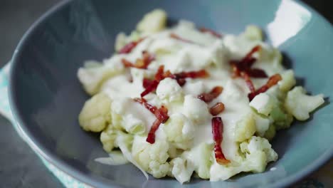 condimento de coliflor cocida en tazón gris con tocino frito y queso bryndza