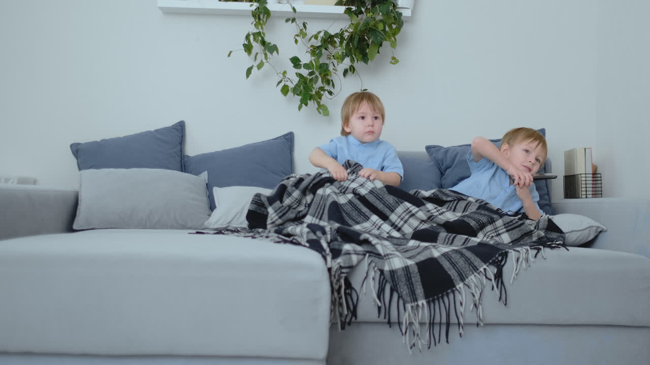 dos niños de 4 y 2 años de edad, están viendo la televisión sentados en el sofá. un emocionante programa de televisión. ver dibujos animados