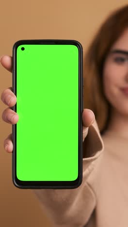 woman showing cellphone with green screen in studio. vertical footage