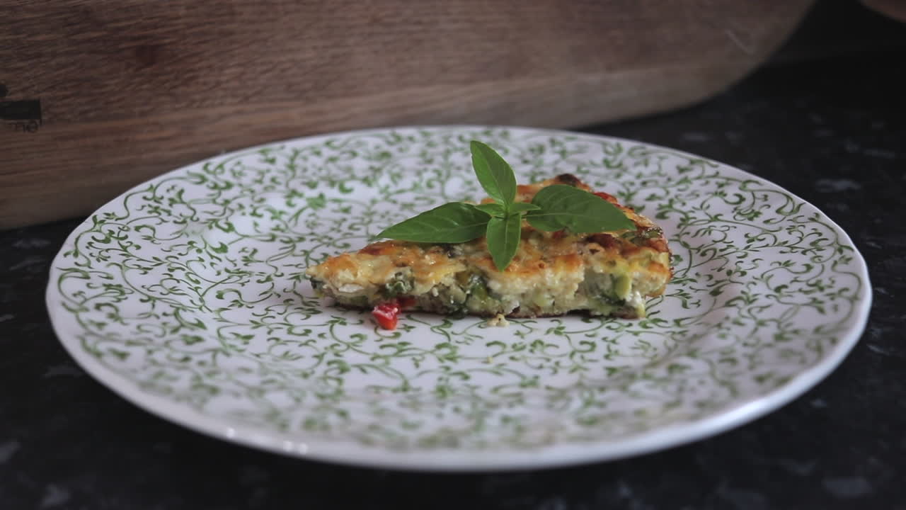 Frittata di pomodoro, peperone rosso, cavolo riccio, zucchina, cipolla e pancetta posizionata su un piatto, con zoom lento in avanti.