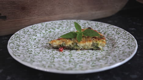 Tomato,-red-pepper,-kale,-zucchini--courgette,-onion-and-bacon-frittata-being-placed-on-plate,-slow-zoom-in